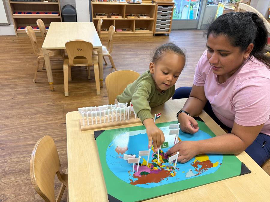 A child and a practitioner placing flags on a world map in the classroom